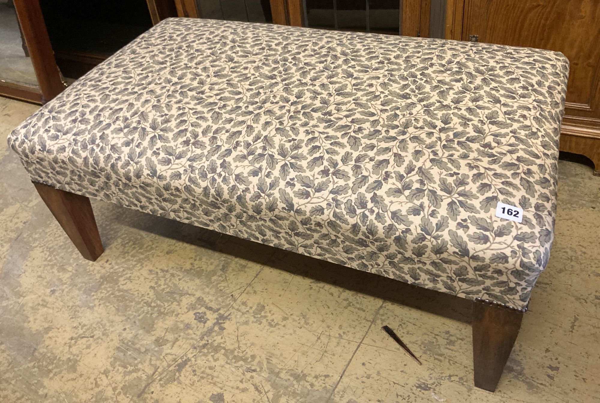 A modern rectangular footstool upholstered in a printed leaf fabric, width 90cm, depth 53cm, height 28cm